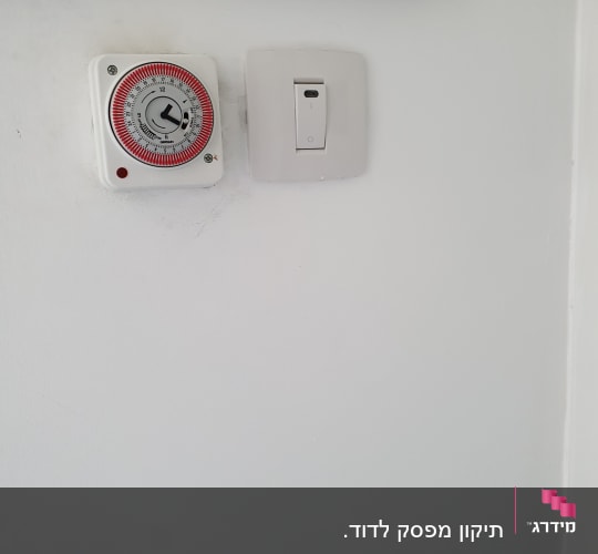 שעון טיימר ומתג חשמלי על קיר לבן